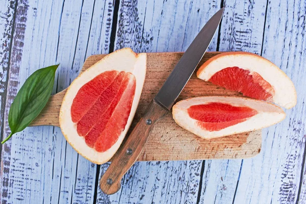 Ripe slice of red grapefruit citrus fruit with thick peel on wooden cutting board with knife. Close up, top view. Vegetarian food, vitamin C, ingredient for food, drinks, skin care.