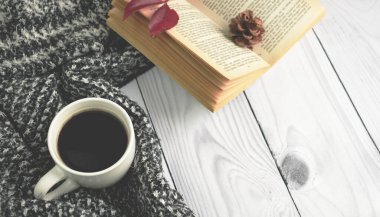 İçinde kitap, çiçek ve kırmızı sonbahar yaprağı olan bir fincan sade kahve ve kahverengi arka planda sıcak yün elbiseler. Düz konum, üst görünüm, kopyalama alanı. Sonbahar kompozisyonu, sonbahar konsepti.