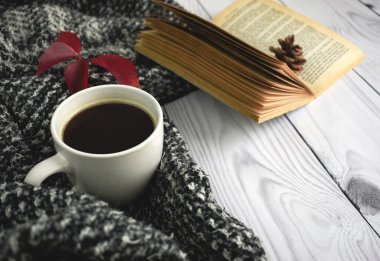 İçinde kitap, çiçek ve kırmızı sonbahar yaprağı olan bir fincan sade kahve ve kahverengi arka planda sıcak yün elbiseler. Düz konum, üst görünüm, kopyalama alanı. Sonbahar kompozisyonu, sonbahar konsepti.