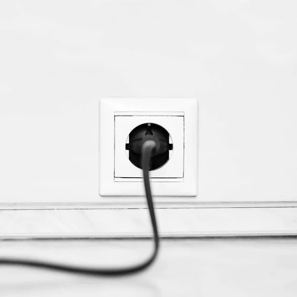 Electric white socket and one plugged in power cord on white wall background