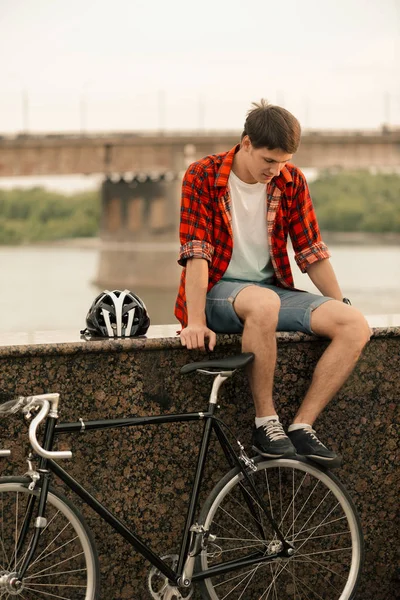 빨간 셔츠를 입은 젊은 남자가 그 근처의 빈티지 자전거로 계단에 앉아 있습니다. — 스톡 사진