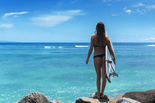 Surfer vrouw dragen bikini met een blauw bord tegen de achtergrond van de Oceaan en blauwe hemel met wolken Stockfoto