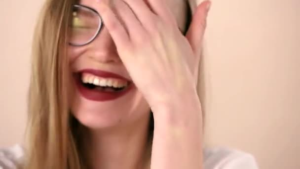 The face of a young emotional happy woman with long blonde hair and glasses. Happily laughs, looking at the camera — Stok video