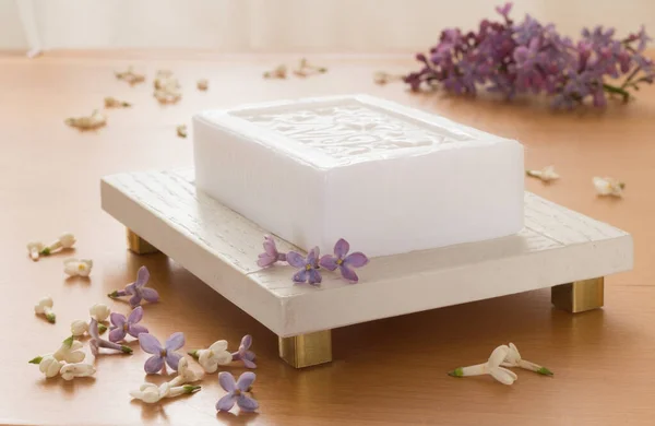 Beyaz sabun ve leylak çiçekleriyle süslenmiş bir sabun. Ahşap arkaplan, arka plan aydınlatma. 