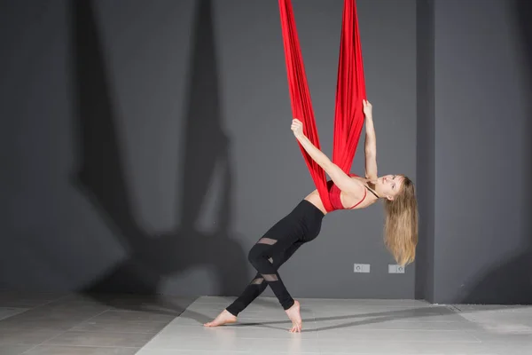 Fly yoga. Young woman practices aerial anti-gravity yoga with a hammock in fitness club on gray background.