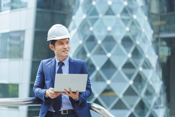 Ingeniero asiático con sombrero duro blanco celebración portátil de trabajo al aire libre lugar . — Foto de Stock
