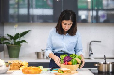 Asyalı kadın mutfakta, yemek masasında bol ekmek ve sebze var..
