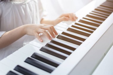 asian beautiful child girl playing electric piano in living room at home. clipart