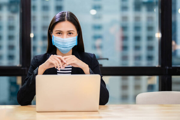 Азиатские женщины носят маски защиты от инфекций, передающихся по воздуху и слюны, во время вспышки вируса Ковид 19 (Коронавирус) и работы с ноутбуком в офисе.
