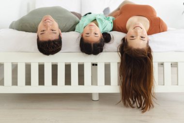 Mutlu Asyalı bir aile tatilde yatak odasında dinleniyor, baba ve kız baş aşağı yatıyorlar..