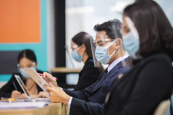 Asian business people wear masks and face shield protect against airborne disease during outbreak of covid-19 or coronavirus meeting conference discussion of workers in office.