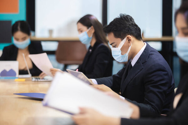 Азиатские бизнесмены надевают маски для защиты от болезней, передающихся воздушно-капельным путем во время вспышки вируса ковид-19 или коронавируса, обсуждают на конференции рабочих в офисе, новый нормальный образ жизни.