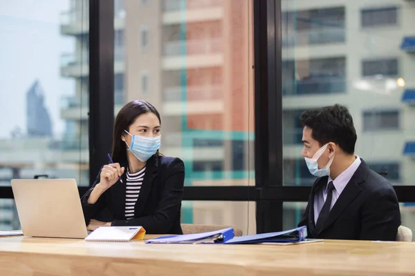 Asian business people wear masks and face shield protect against airborne disease during outbreak of Covid-19 or coronavirus, sitting working social distance from work in office.