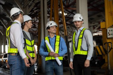 Güvenlik kasketi takmış bir grup mühendis ve iş adamı endüstriyel bir fabrikada tartışıyorlar. Takım çalışması kavramı, saha toplantısı, mühendislik yönetimi ve işbirliği.