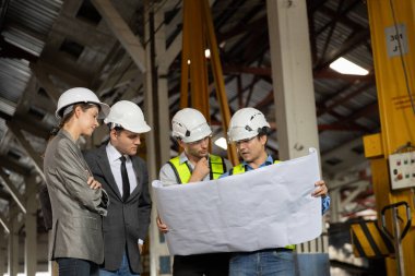 Bir grup demiryolu mühendisi ve güvenlik kaskı takmış iş adamları bir sanayi fabrikasının planlarını gözden geçiriyorlar. Proje planlama, beyin fırtınası ve mühendislik takım çalışması kavramı.