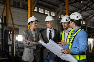 Bir grup demiryolu mühendisi ve güvenlik kaskı takmış iş adamları bir sanayi fabrikasının planlarını gözden geçiriyorlar. Proje planlama, beyin fırtınası ve mühendislik takım çalışması kavramı.