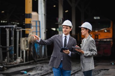 Güvenlik kaskı takan, dijital tablet kullanan ve demiryolunda tartışan iki iş adamı. Endüstriyel liderlik kavramı, saha teftişi, yönetim ve planlama.