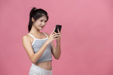 Genç Asyalı kadınlar mutlu ifadeli akıllı telefon kullanıyor, iletişimi, teknolojiyi, sosyal medyayı veya pembe arka planda online yaşam tarzını sembolize ediyor, dijital kavramlar için mükemmel..