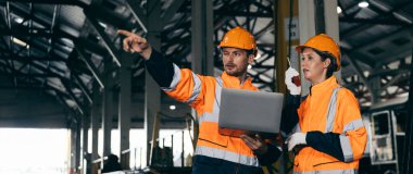 Güvenlik kaskı ve turuncu yansıtıcı ceket giyen iki mühendis, tren bakımını kontrol ederek, takım çalışması, güvenlik ve ulaşım ve takım çalışmasını temsil eden endüstriyel işlemleri tartışıyor..