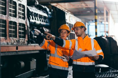 Güvenlik teçhizatı ve miğfer takan iki mühendis demiryolu bakım tesisinde makineleri denetliyor, ekip çalışması, makine mühendisliği ve demiryolu sistem teftişi.