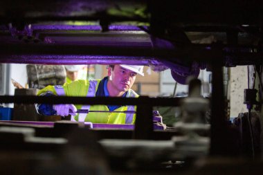 Güvenlik teçhizatı ve miğfer takan iki mühendis demiryolu bakım tesisinde makineleri denetliyor, ekip çalışması, makine mühendisliği ve demiryolu sistem teftişi.