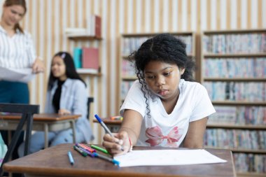 Sınıfta masasında renkli kalemlerle resim çizen Afro-Amerikan öğrenci. Yaratıcılık, konsantrasyon, çocukluk eğitimi ve okul ortamında bireysel öğrenme kavramı.