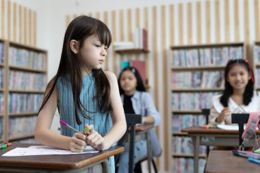 Sınıfta masada oturan üzgün genç kız, arka plandaki diğer öğrencilere bakmıyor. Zorbalık, yalnızlık, çocukluk duygusu ya da okul ortamında sosyal dışlanma kavramı.