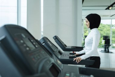 Spor başörtüsü içindeki Müslüman kadınlar spor salonunda koşu bandında duruyorlar, kardiyo egzersizine hazırlanıyorlar, fitness, sağlık, aktif İslam yaşam tarzı, refah ve spordaki kültürel çeşitliliği sembolize ediyorlar..