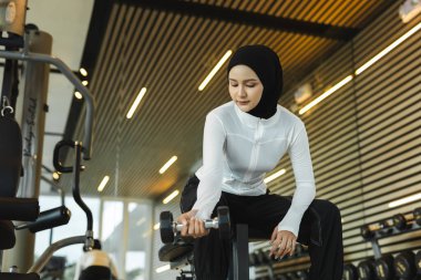 Spor kıyafetli Müslüman bir kadın spor salonunda dambılı kaldırıyor. Güç eğitimi, zindelik, sağlıklı yaşam tarzı ve aktif yaşamda güçlü İslamcı kadınlar için fiziksel egzersiz kavramı.