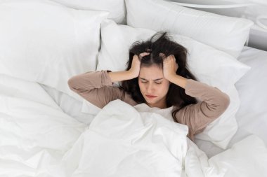 Yatakta gözleri kapalı yatan genç kadınlar, sabahları baş ağrısı ya da stres hissediyorlar. Uyku bozukluğu, migren ya da endişe kavramı. Doğal ışık, yumuşak yatak.