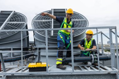 Güvenlik teçhizatı olan mühendisler çatıdaki havalandırmayı ve güneş paneli sistemlerini enerji verimliliği için inceliyorlar. Endüstriyel bakım, temiz enerji ve tesis yönetimi kavramı.