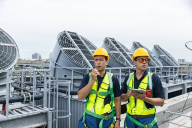 Çelik yelek ve kask giyen mühendisler çatıda HVAC sistem denetimini tartışıyor. Endüstriyel bakım ve havalandırma sistemi işletim konsepti.