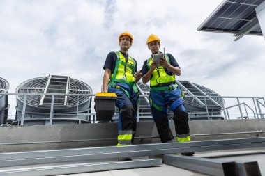 Güvenlik teçhizatı olan mühendisler çatıdaki havalandırmayı ve güneş paneli sistemlerini enerji verimliliği için inceliyorlar. Endüstriyel bakım, temiz enerji ve tesis yönetimi kavramı.