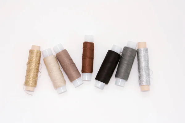 Flat lay colorful cotton thread spools, embroidery yarn, white, brown, gray, black, silver, gold bobbins, mock up, top view. Layout mockup, blank white background for needlework, sewing poster, banner