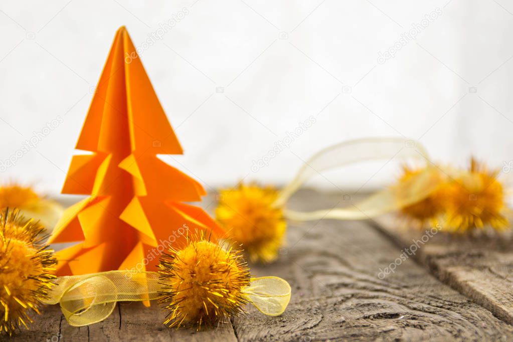 Orange origami tree with shiny balls on a wooden base with a white background.