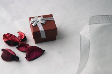 Sevgililer günü! Kırmızı kutu gümüş şerit ve beyaz bir arka plan üzerinde izole kuru kırmızı yaprakları ile bir hediye için. Üstten görünüm.