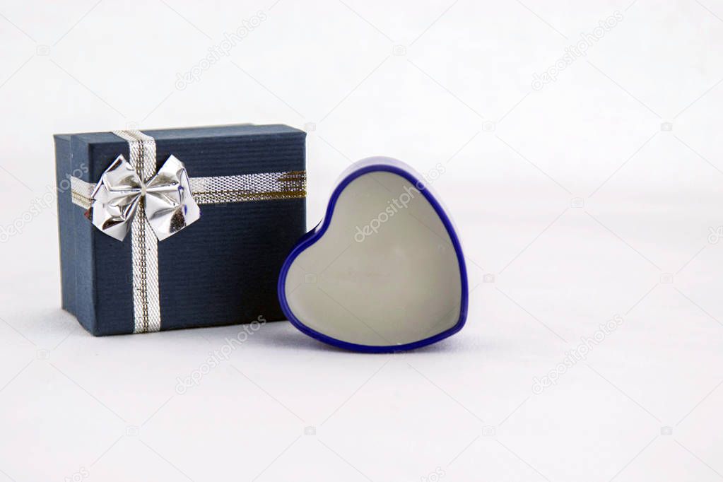 Valentines day concept. Decorative blue heart  and a blue  gift box with silver ribbon on a white background. Close up.