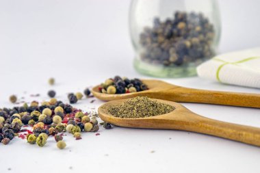 Beyaz bir arka planda ahşap bir kaşık tahıl ve toprak karabiber renkli biber