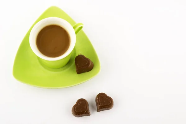 Coffee in a green cup with chocolate in the shape of a heart on a white background. Top view.