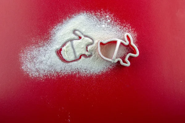 Red mold in the shape of bunnies sprinkled flour on red background