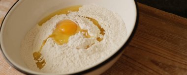 Kapatın. Pasta yapıyorum. Beyaz un tepesinde sarı yumurta kasesi.,