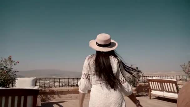 En pen, ung brunette med europeisk utseende i en hvit, vakker kjole løper på terrassen på veien, snurrer og ser på utsikten – stockvideo