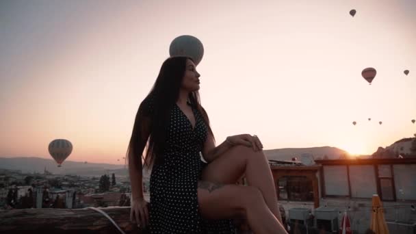 ヨーロッパ風の美しいブルネットはカッパドキアの日没時に気球のテラスの背景に座っています — ストック動画