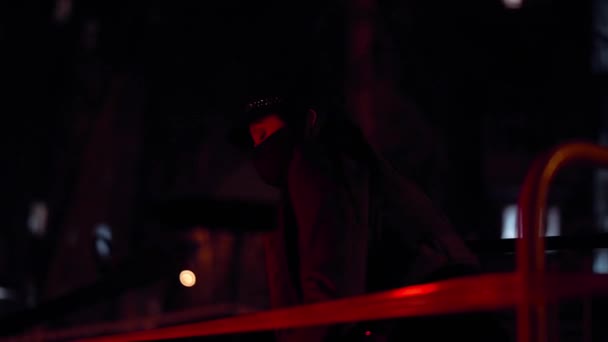 Девушка в черной маске вируса сидит за оградой ленты смотрит в камеру в красном свете — стоковое видео