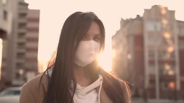 Bella ragazza con un cappotto beige in maschera virale bianca sta al vento — Video Stock