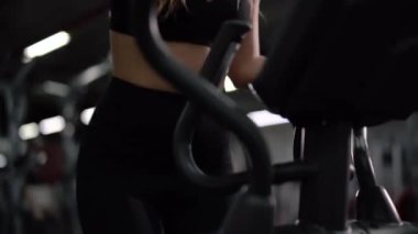 Siyah bir konudaki zayıf atletik kız elipsoid simülatörde kardiyo yapıyor.