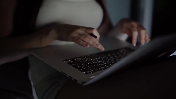 Дівчина в білій футболці і джинсових шортах працює на ноутбуці пізно вночі на підвіконні — стокове відео