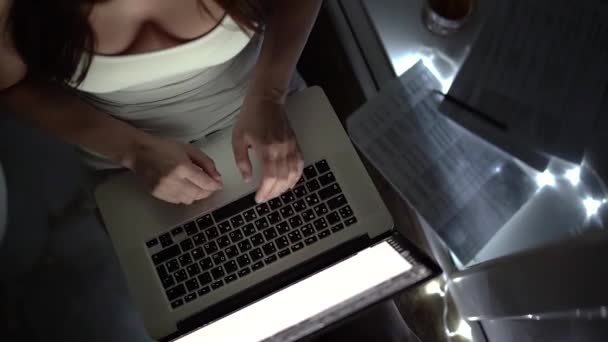 Дівчина в білій футболці працює на ноутбуці пізно вночі на підвіконні — стокове відео