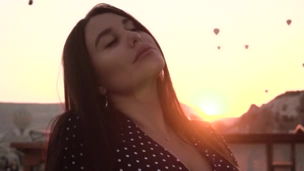 Gyönyörű barna, európai megjelenésű ül a teraszon hátterében egy léggömb naplementekor Cappadocia — Stock videók