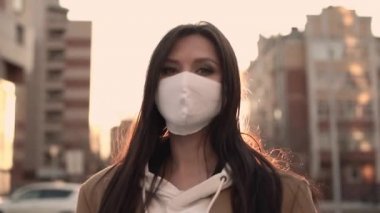 Beyaz viral maskeli bej ceketli kız rüzgârda duruyor.